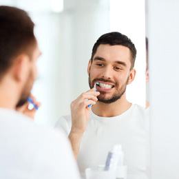 Bearded man brushing his teeth in the mirror