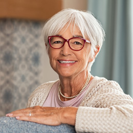 Senior woman with glasses smiling while turned around on couch