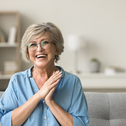 Senior woman on couch smiling and clapping hands together