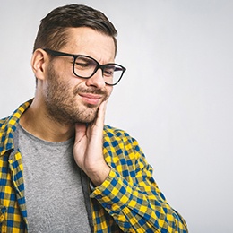 Man with glasses rubbing his jaw due to discomfort
